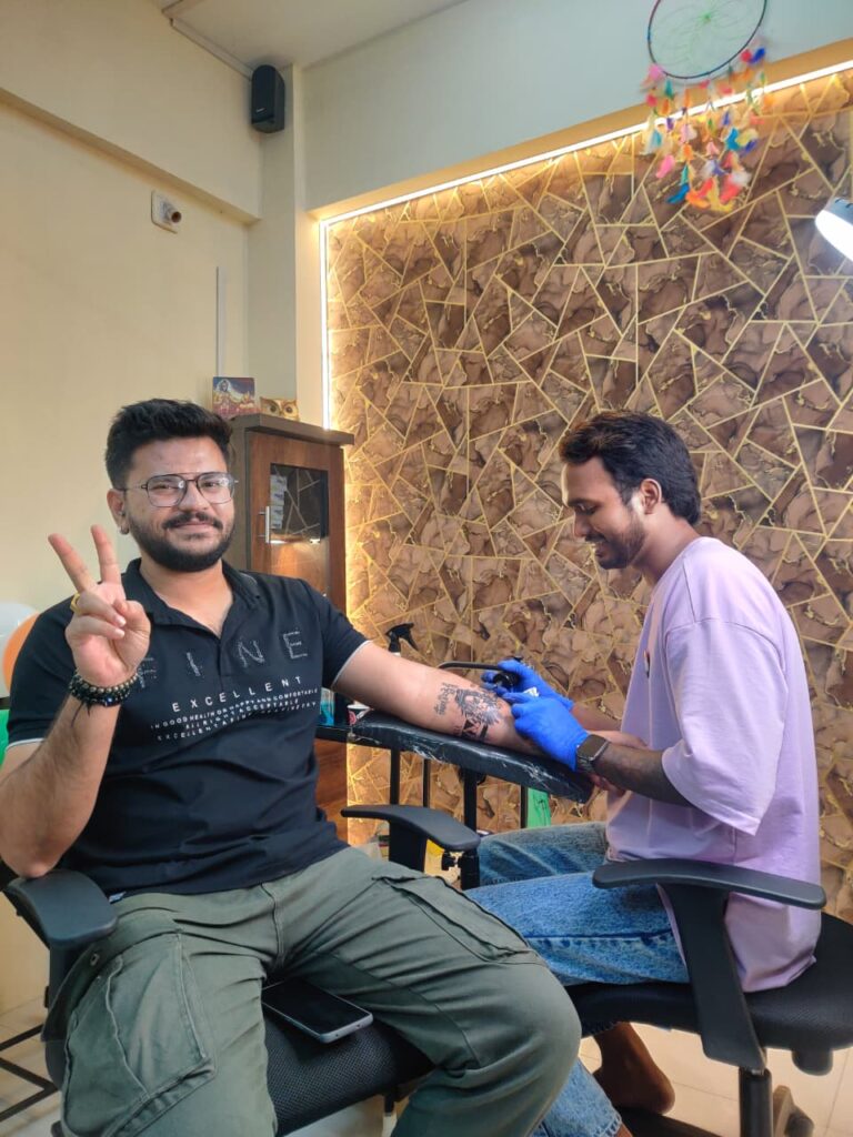 Tattoo shops in Surat – artist making band tattoo, smiling client